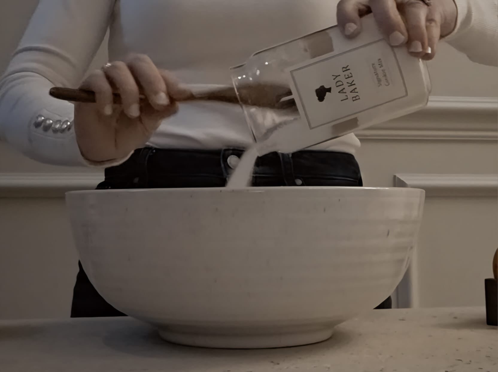 Woman pouring Lady Baker baking mix from jar into a large mixing bowl