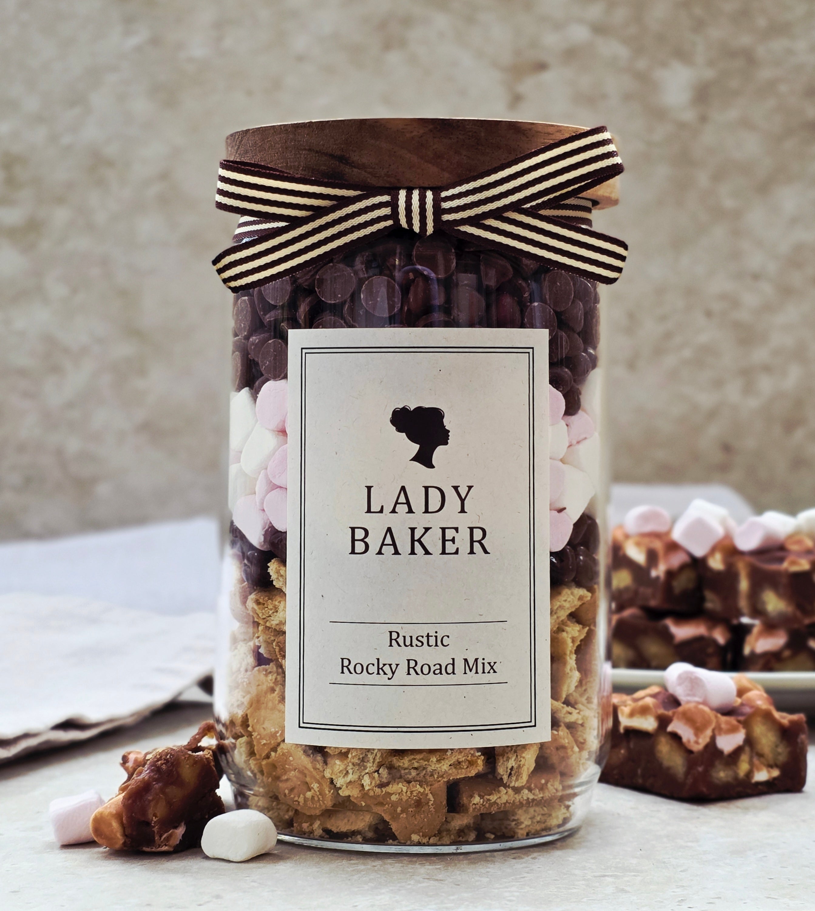 Lady Baker glass Jar of Lady Baker Rustic Rocky Road Mix with a decorative bow on a neutral background
