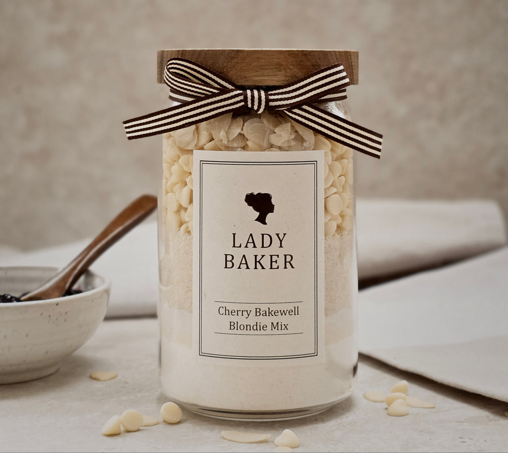 Lady Baker glass Jar of Lady Baker Cherry Bakewell Blondie Mix with a ribbon on a neutral background
