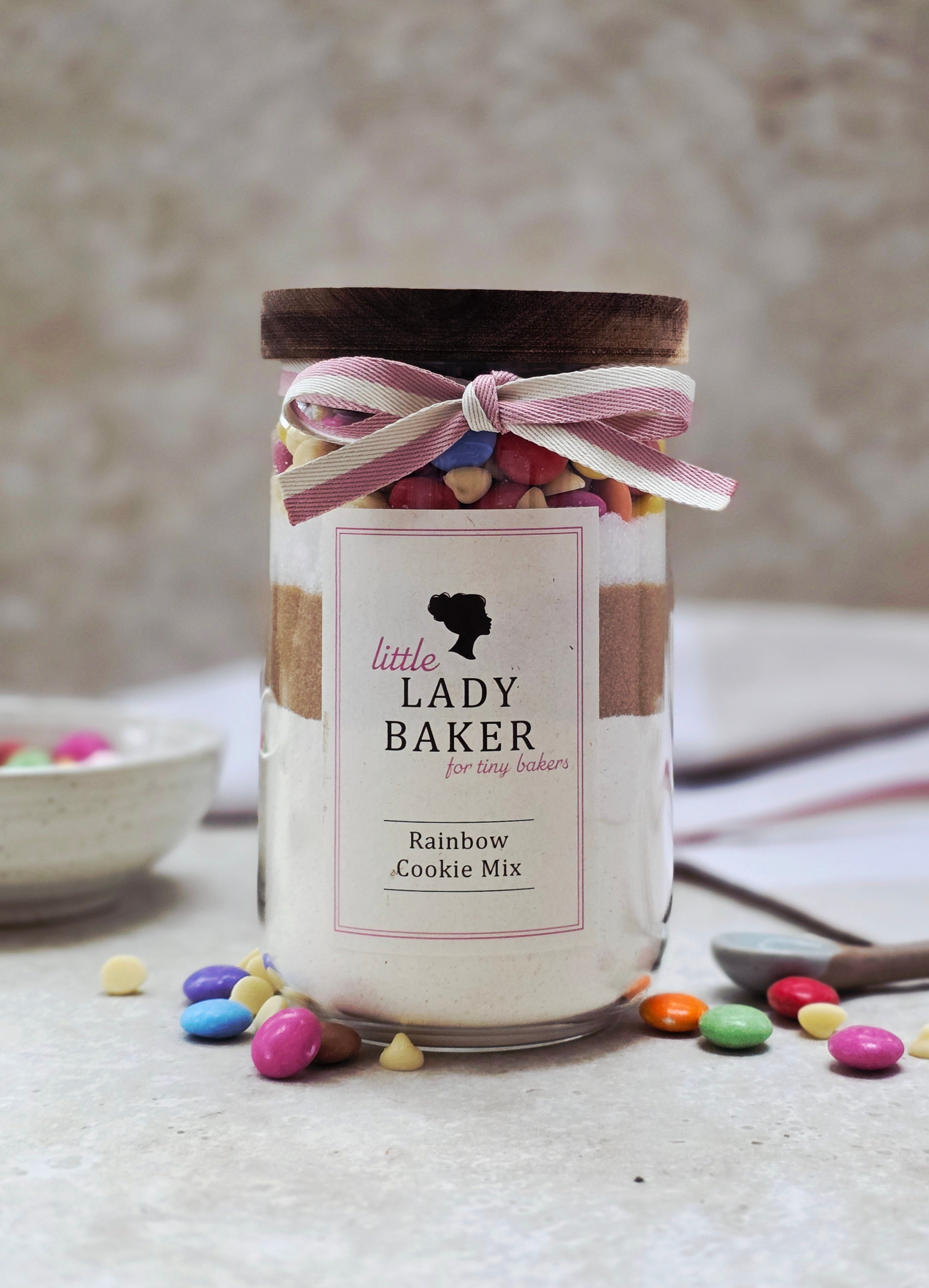 Lady Baker glass jar of rainbow cookie mix with a decorative ribbon on a neutral background
