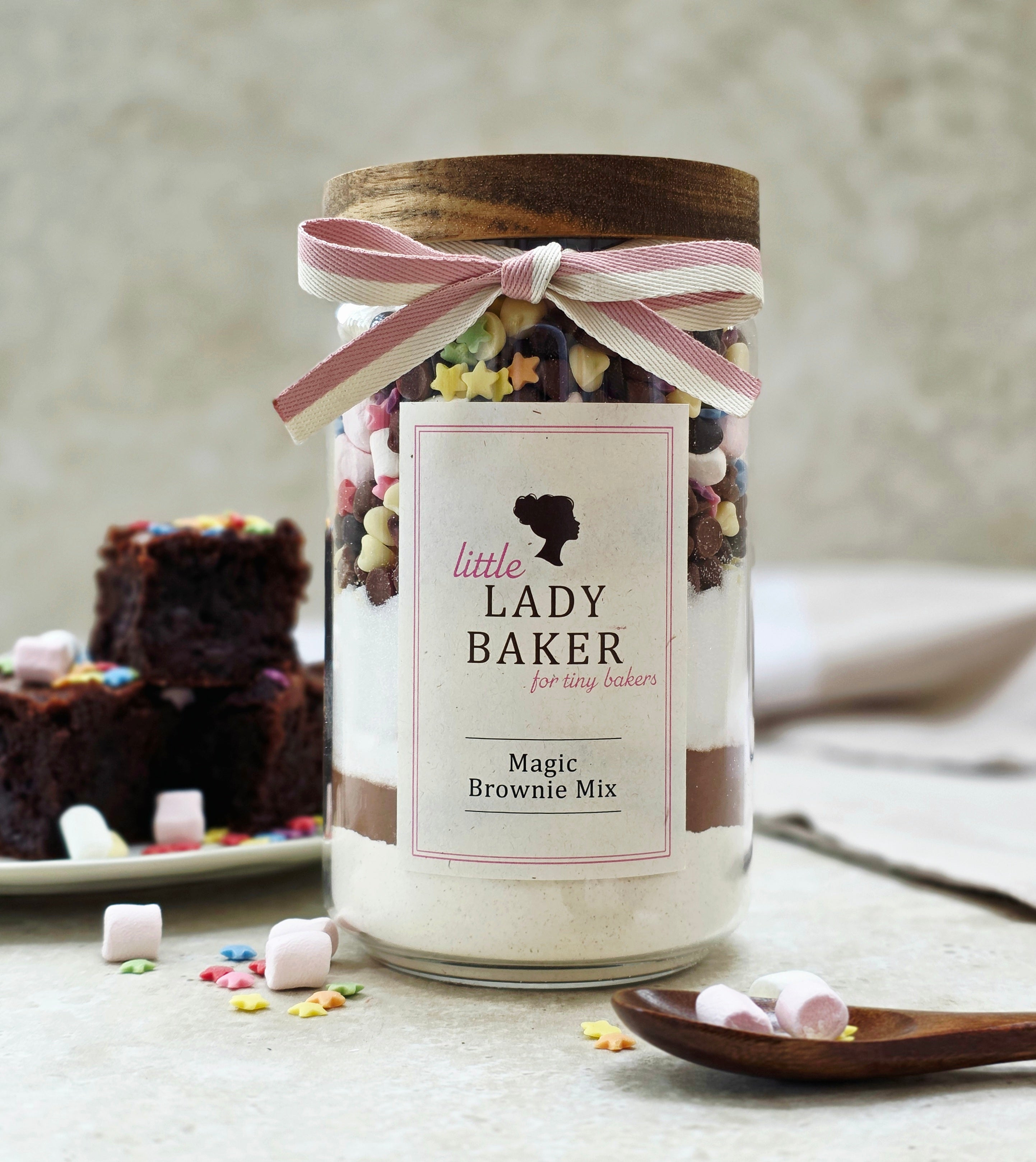 Lady Baker glass jar of magic brownie mix with a label and ribbon, surrounded by baking ingredients.